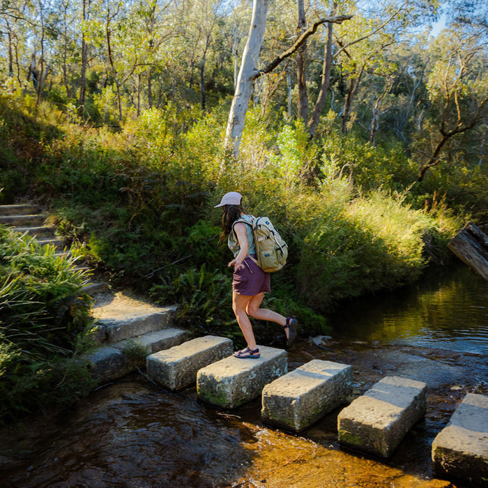 Person with a backpack crossing stepping stones over a stream in a forest