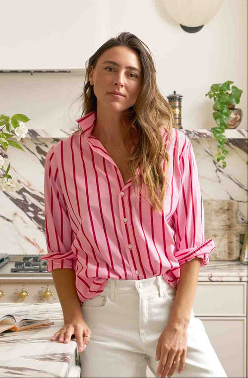 Woman in a pink striped shirt and white pants standing in a modern kitchen.