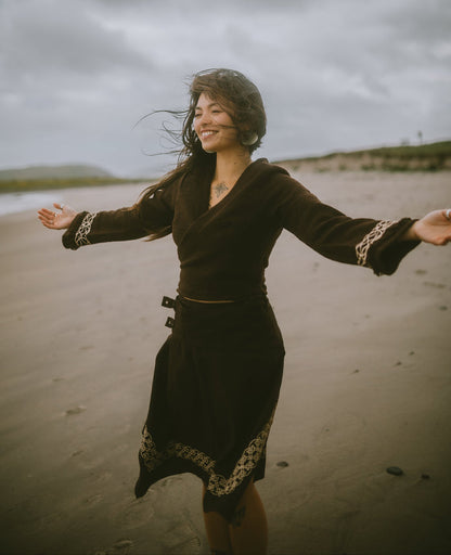 Brown folklore crop top with adjustable wrap fit and Celtic embroidered cuffs designed by Celtic Fusion and styled on a moody coastal beach with windswept hair