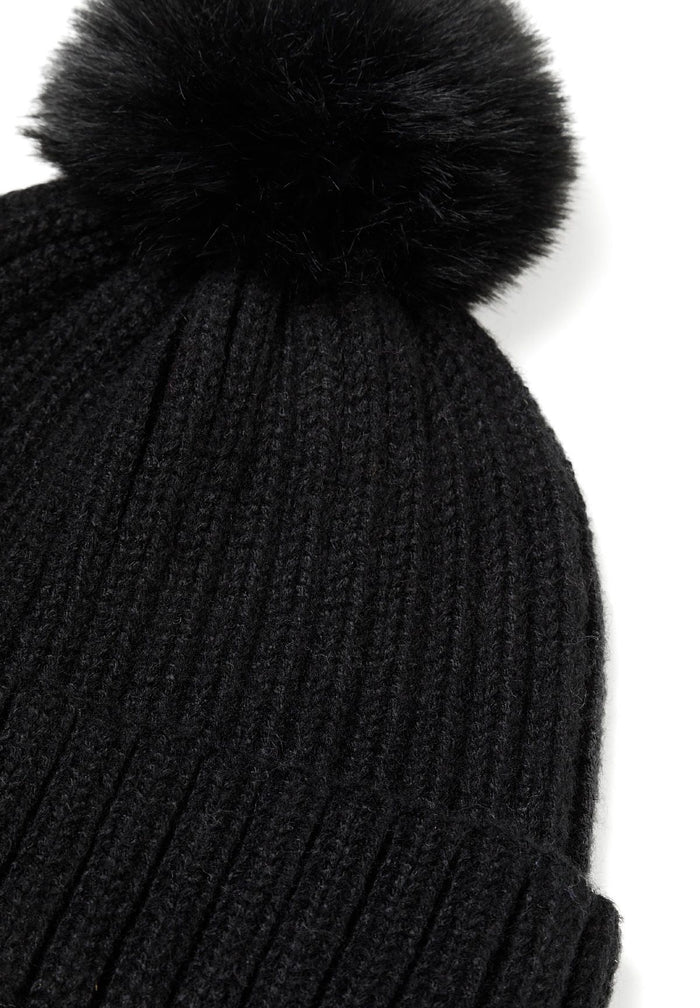 Close-up of a black knitted beanie hat with a faux fur pom pom and ribbed texture.