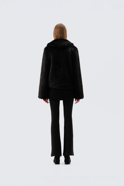 Black faux fur jacket with notch lapel and cropped fit, worn open over a black top and flared trousers, back view
