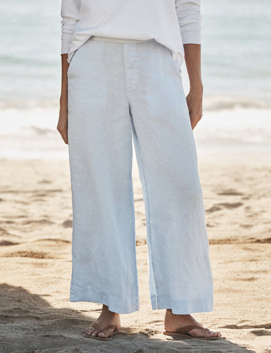 Person wearing light blue wide-leg pants and a white top on a sandy beach.