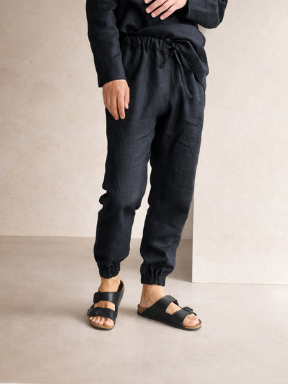 Person wearing black jogger pants and sandals on a neutral background